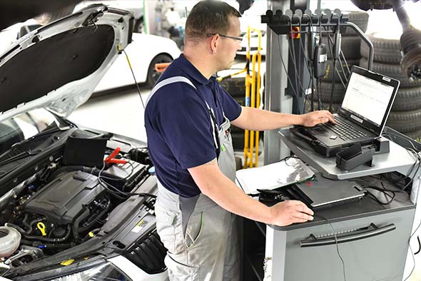 car mechanic maintains a vehicle with the help of a diagnostic computer - modern technology in the car repair shop